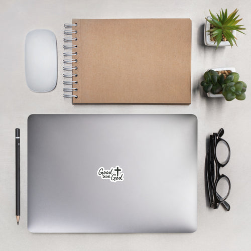 Good With God 3x3 kiss-cut vinyl sticker with white cross logo on a laptop lid surrounded by office supplies in a modern desk lifestyle shot.