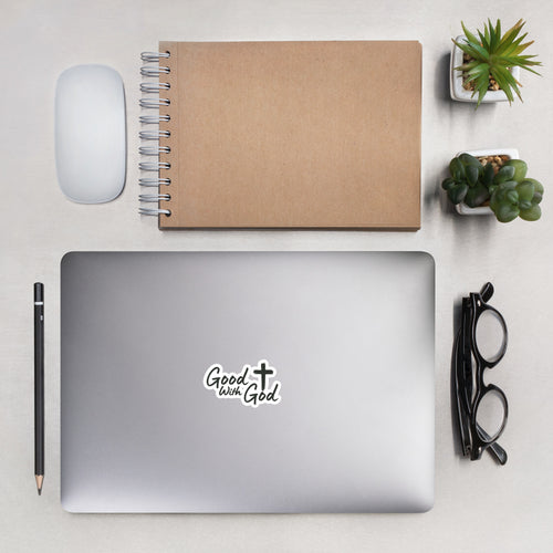 Good With God 4x4 kiss-cut vinyl sticker with white cross logo on a laptop lid surrounded by office supplies in a modern desk lifestyle shot.
